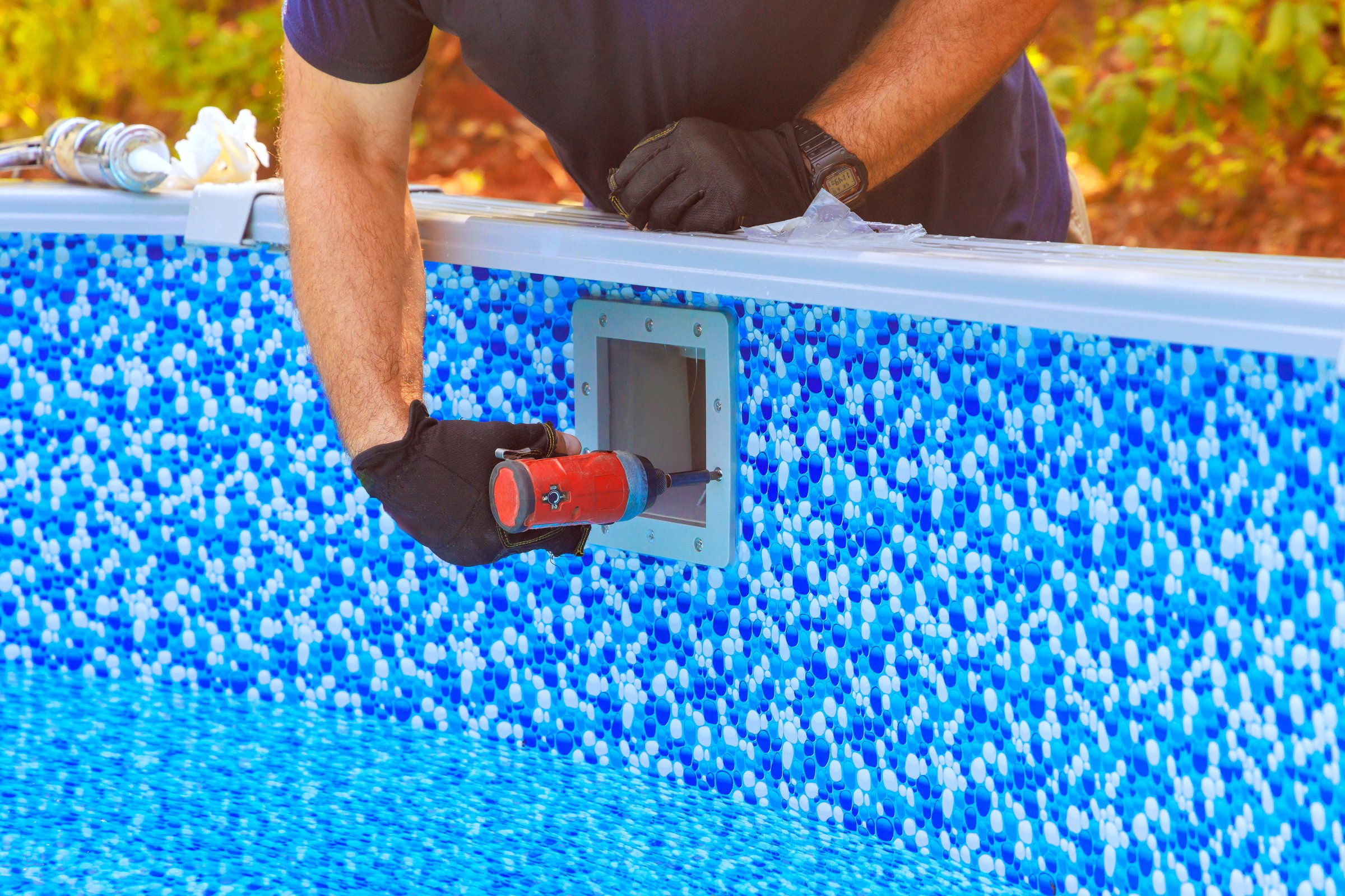 Worker is fixing pool filtration system equipment by edge of blue patterned swimming pool
