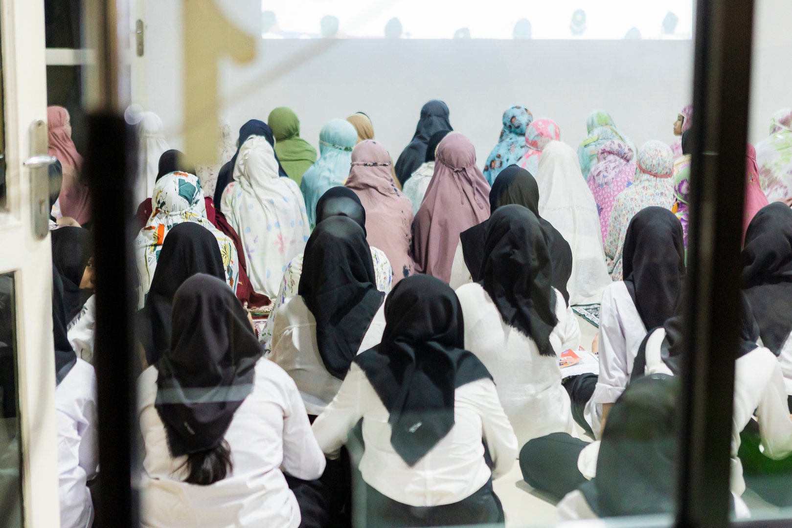 Group of Indonesian women wearing hijabs, sitting on the floor and attentively listening to a speaker during a conference, fostering community and promoting education and learning together