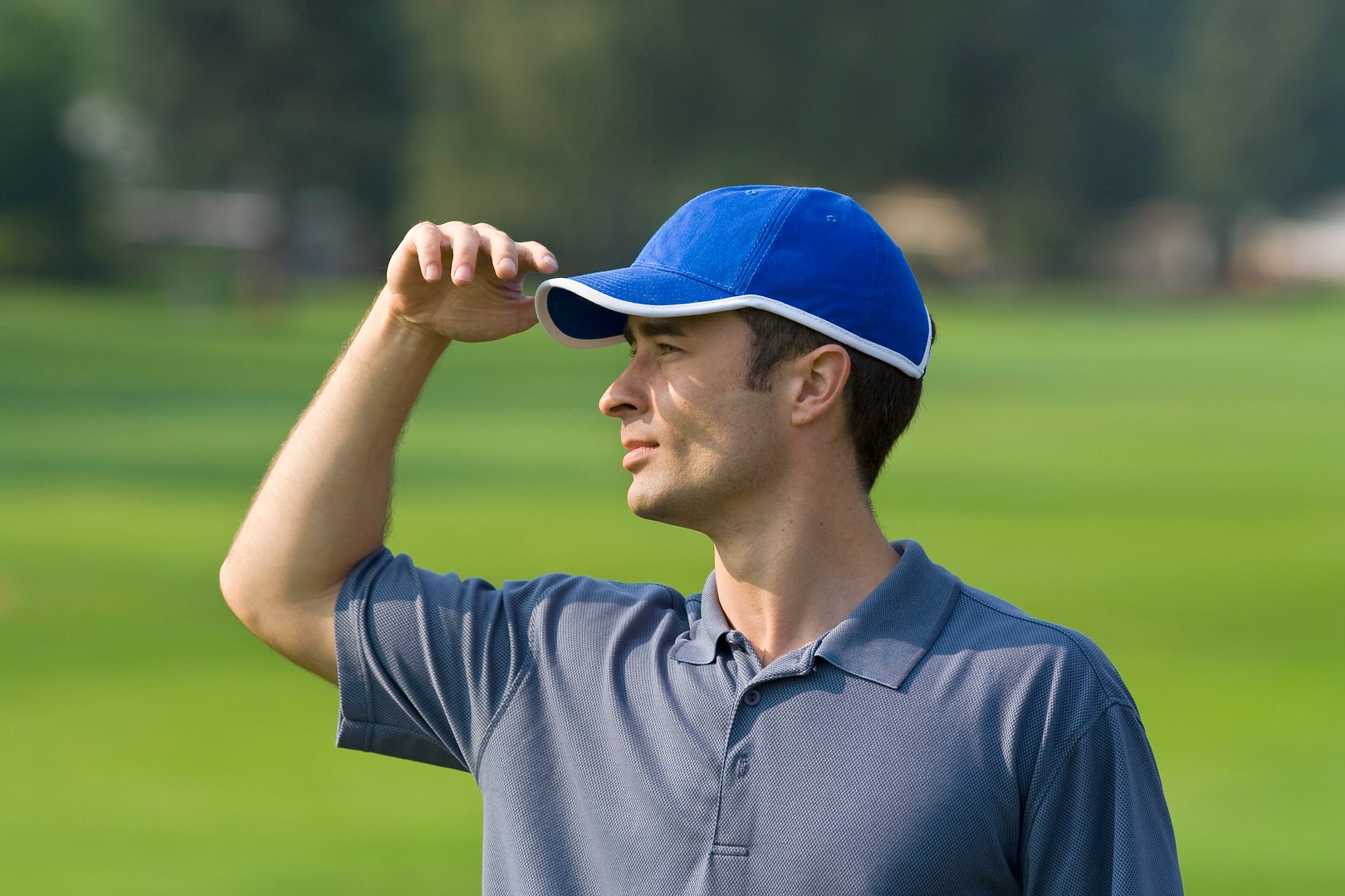 Man's profile while standing on golf course shielding eyes from sun