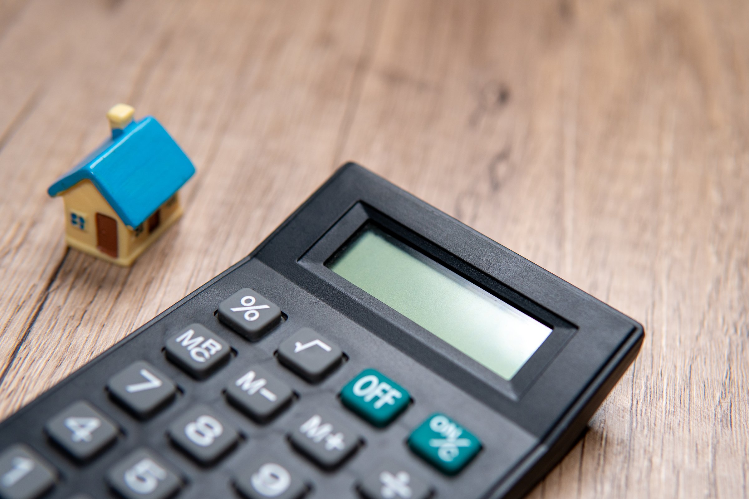 A miniature house next to a black calculator. Copy space for text. Home ownership, financial planning, budgeting concept.