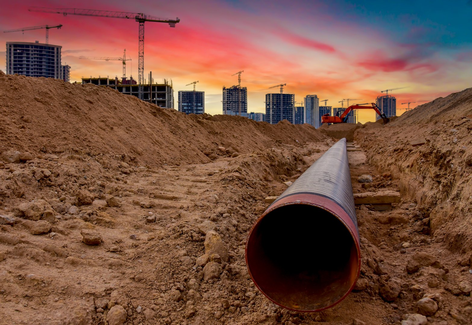 Excavator dig trench on construction site. Laying external sewer pipes in trench. Sewage drainage for building. Civil infrastructure pipe, water lines, sanitary storm. Crane on building construction.