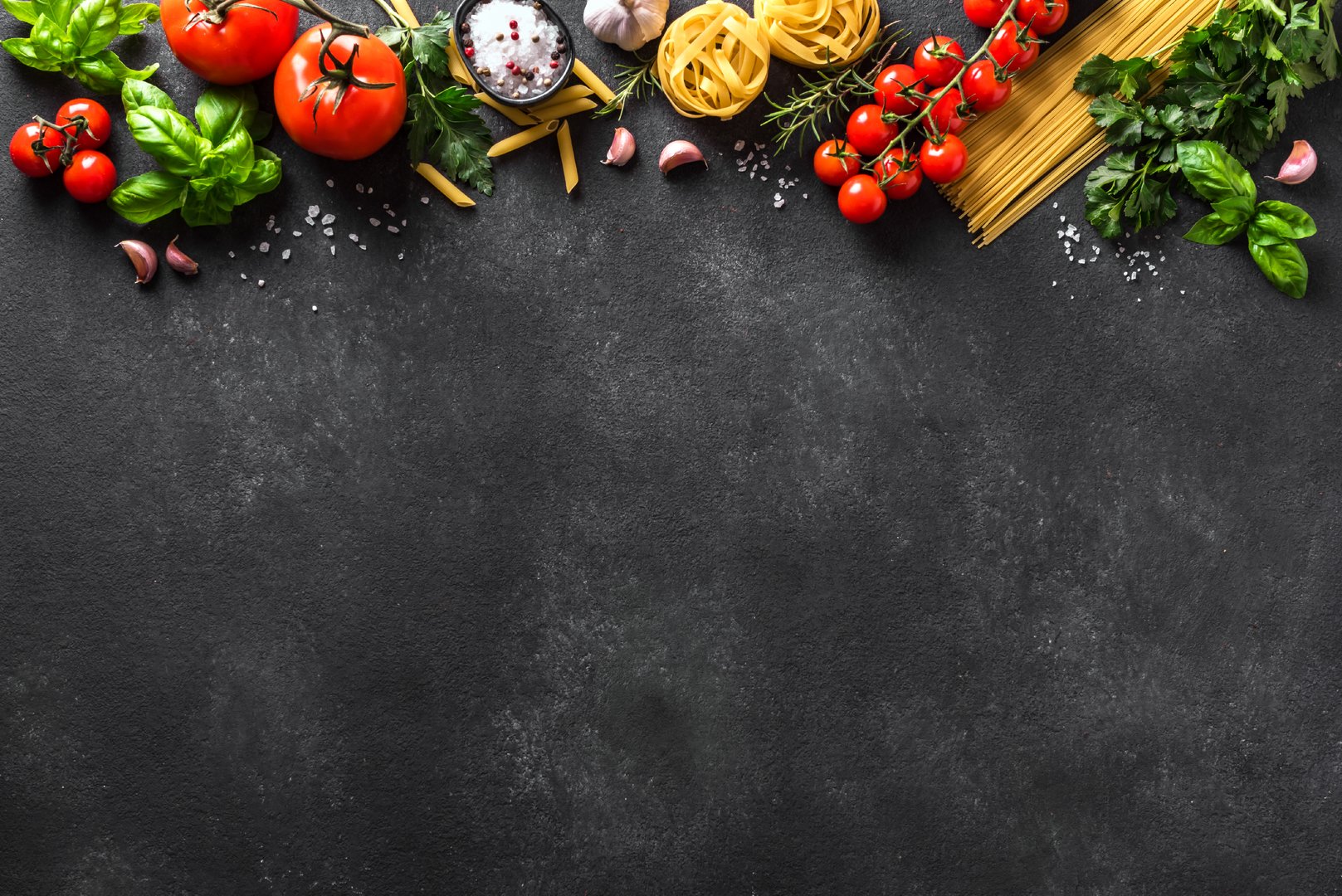Uncooked pasta and vegetables cooking background, top view, copy space. Various italian pasta, tomatoes, basil herbs and spices, italian cuisine concept.
