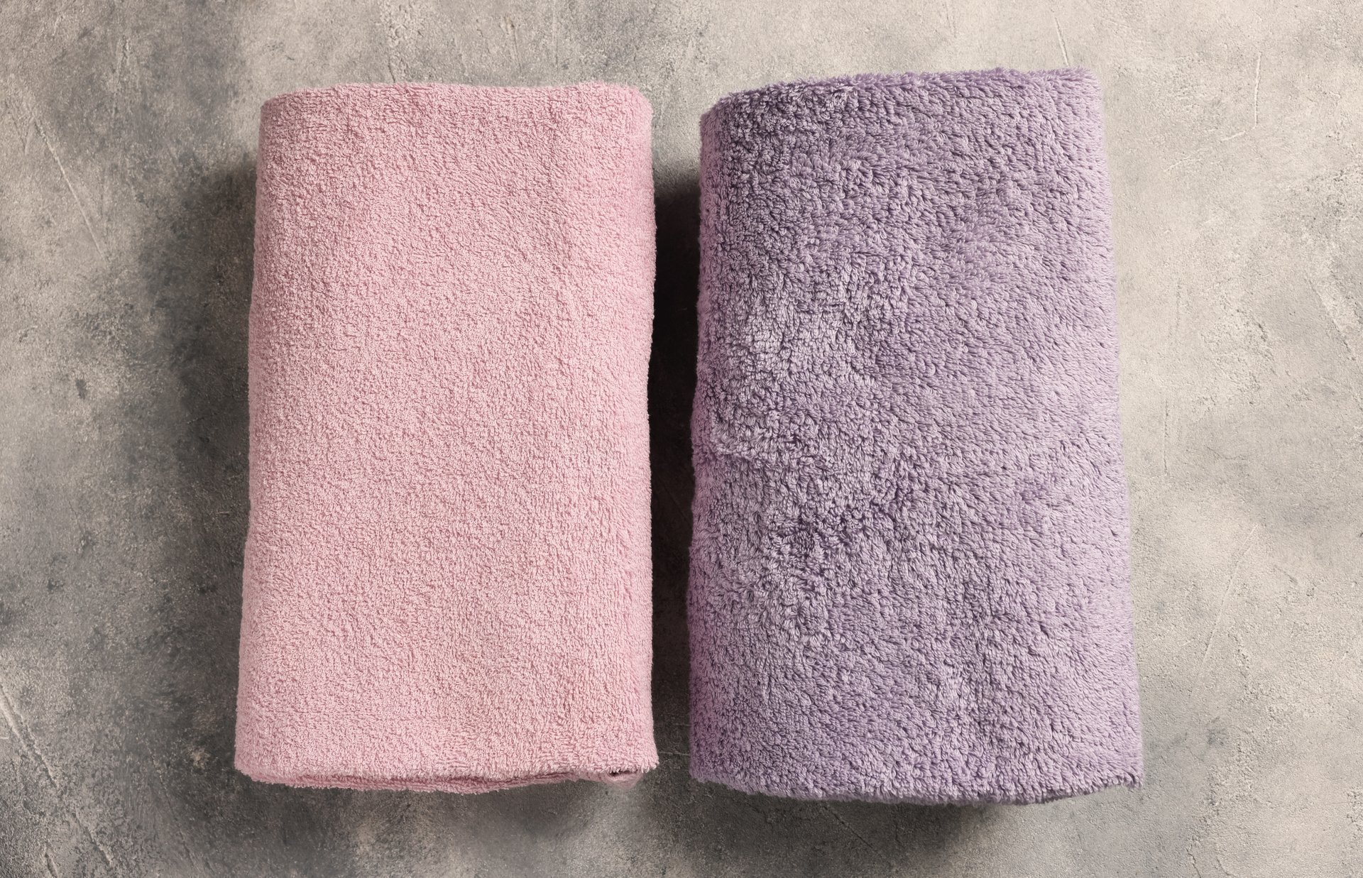 Soft folded terry towels on light gray textured background, flat lay