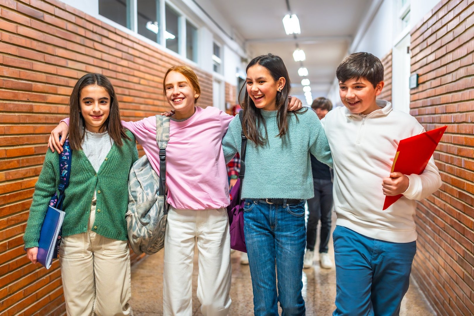 Four cheerful students walking together down the school hallway, embracing each other and sharing smiles, radiate happiness and friendship