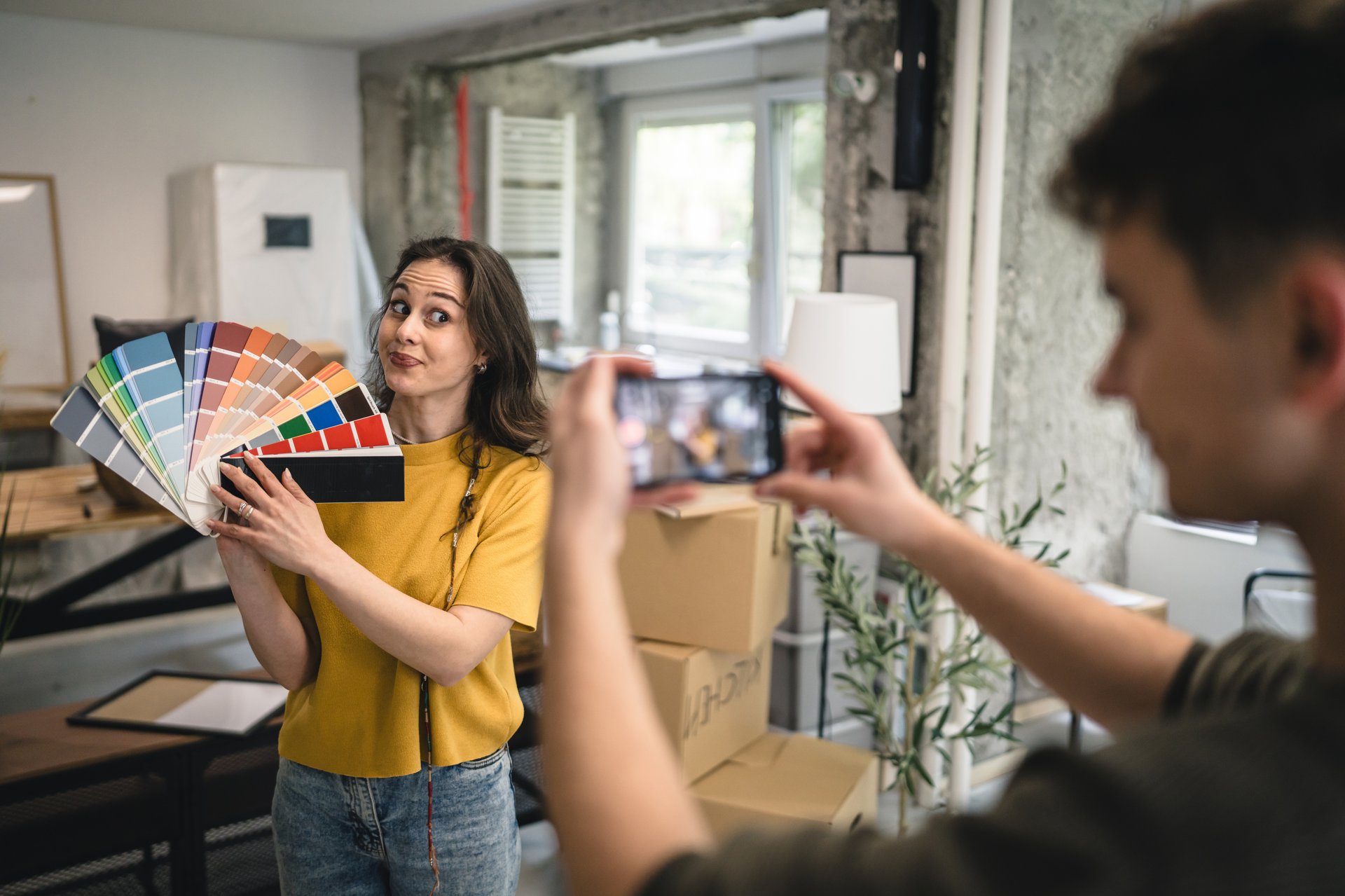 man record video on mobile phone of woman choose color for wall from color palette