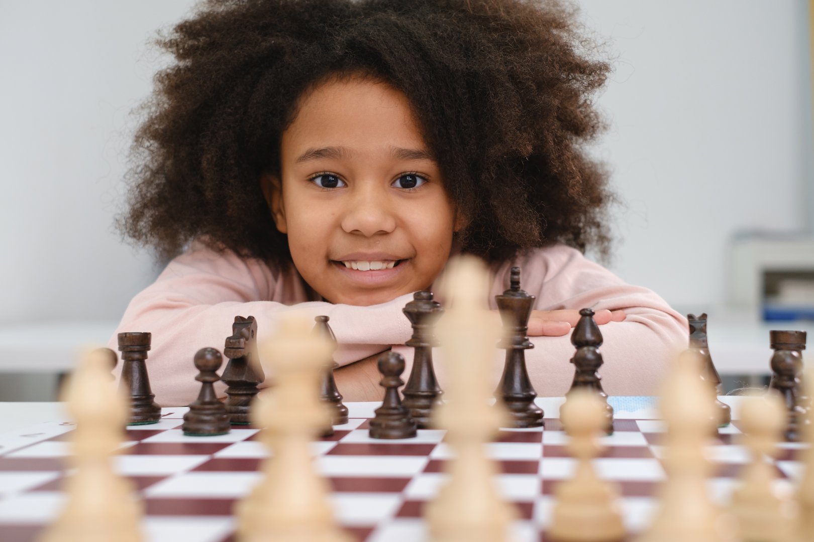 African American girl playing chess. Happy smiling child behind chess smiling in class or school lesson. Excited clever black kid with board game close-up