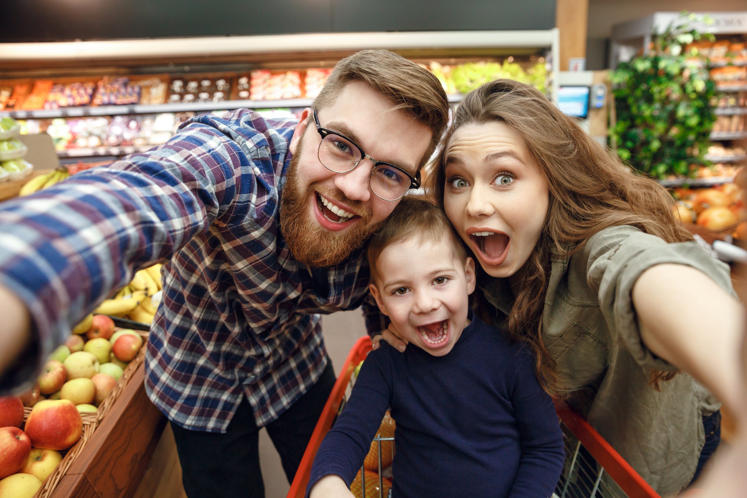 Happy young family making photo in supermarket and looking at the camera