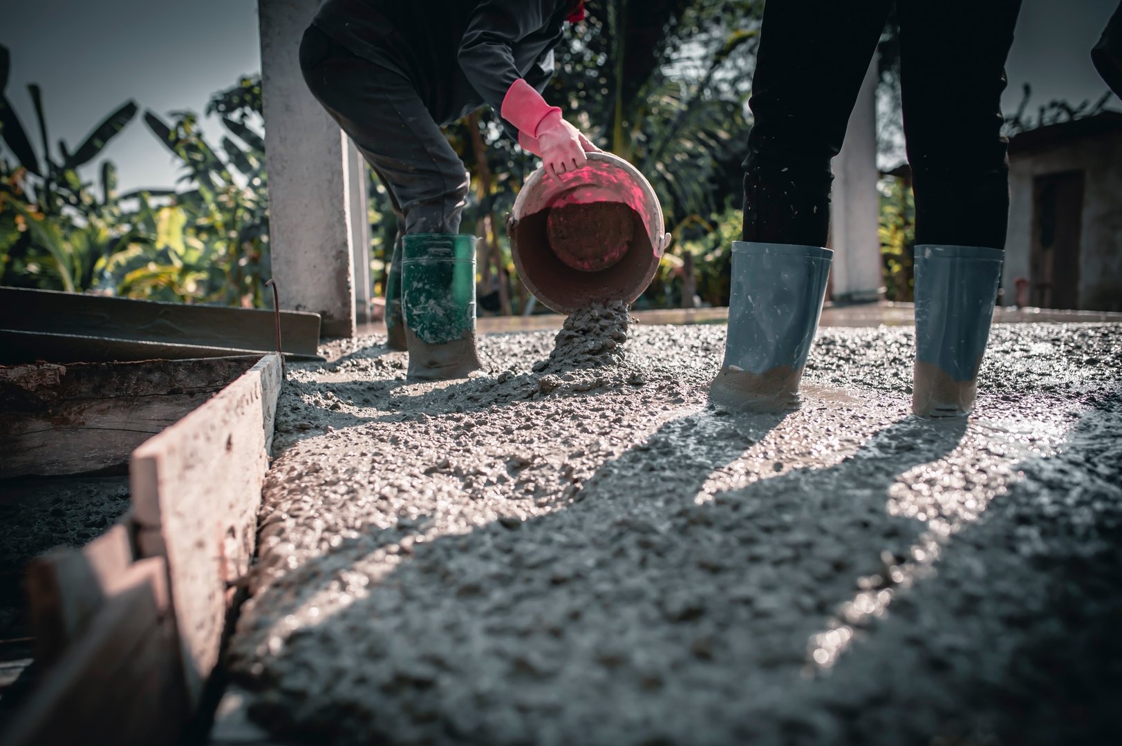 Manually pouring concrete for a surface adjustment on a construction site.