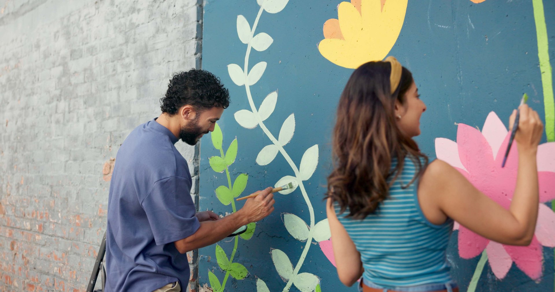 Smile, creative and couple painting on wall for art project, mural design and renovation of community. Happy, people and artist hobby for improvement, diy decoration and makeover for flower aesthetic