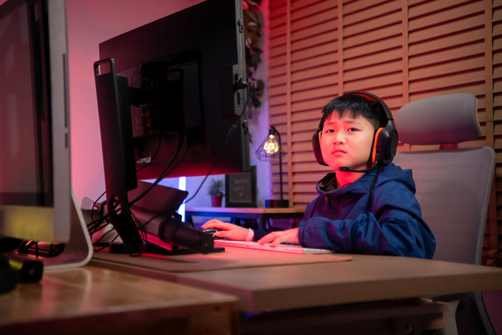 A boy gamer wearing headphones and playing on a desktop computer in a colorful gaming setup