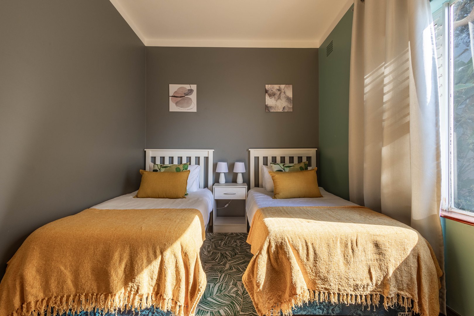 A cozy bedroom with two single beds, matching yellow throws, decorative pillows, and a small nightstand with lamps.
