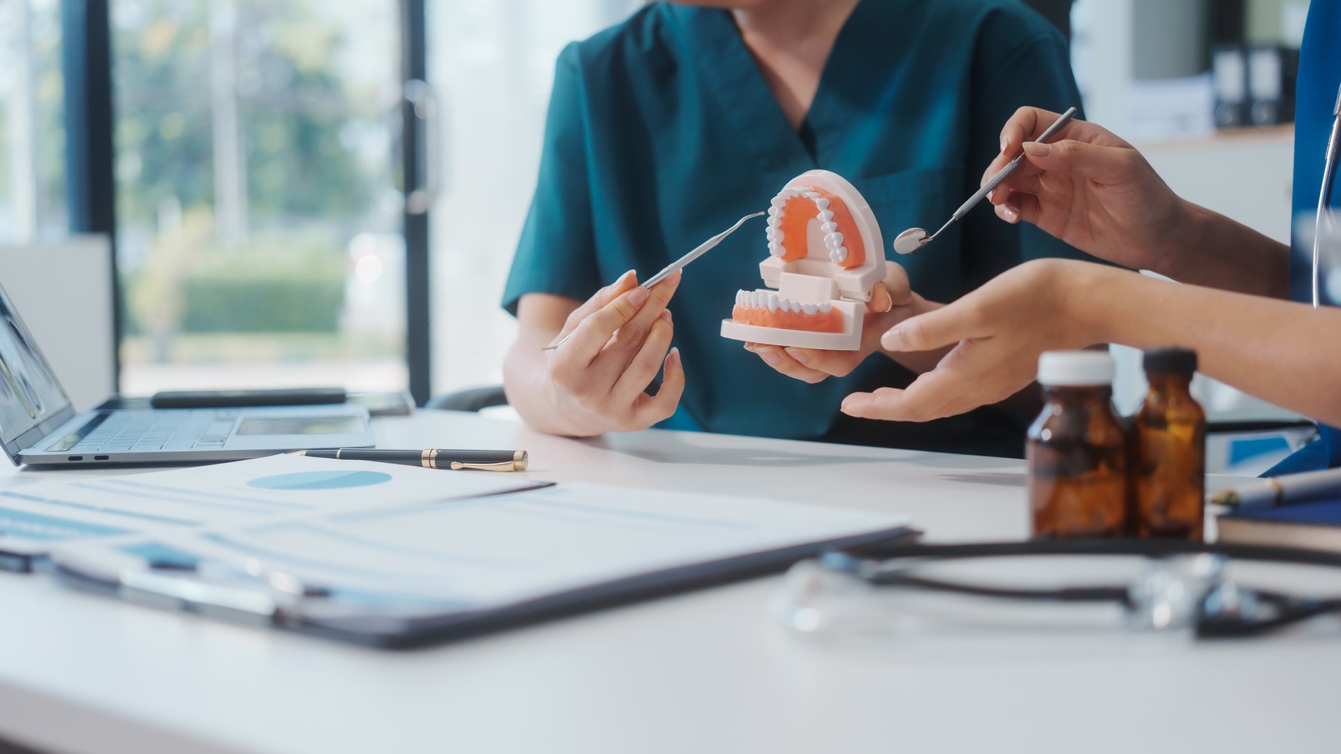 Two Asian female doctors meet at a table in a clinic, with a dentist explaining dental transplantation using a model, discussing treatment, prevention, and patient health for effective oral care