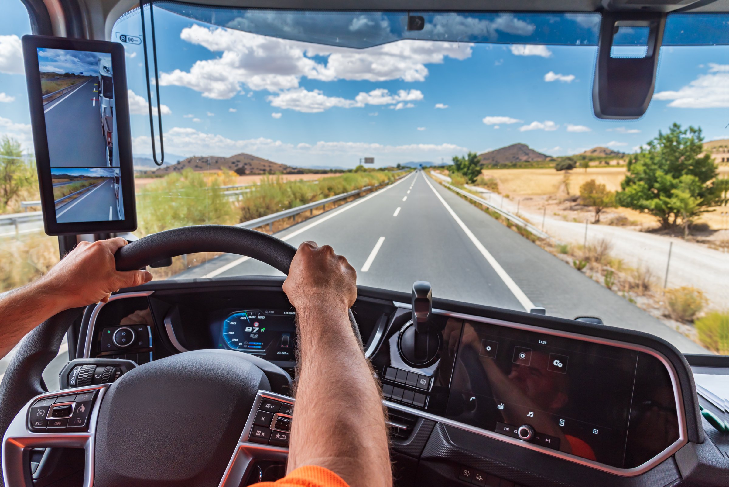 From inside the cab of a truck, driver holding the steering wheel firmly while driving on a straight highway, usually where fatigue increases the most.