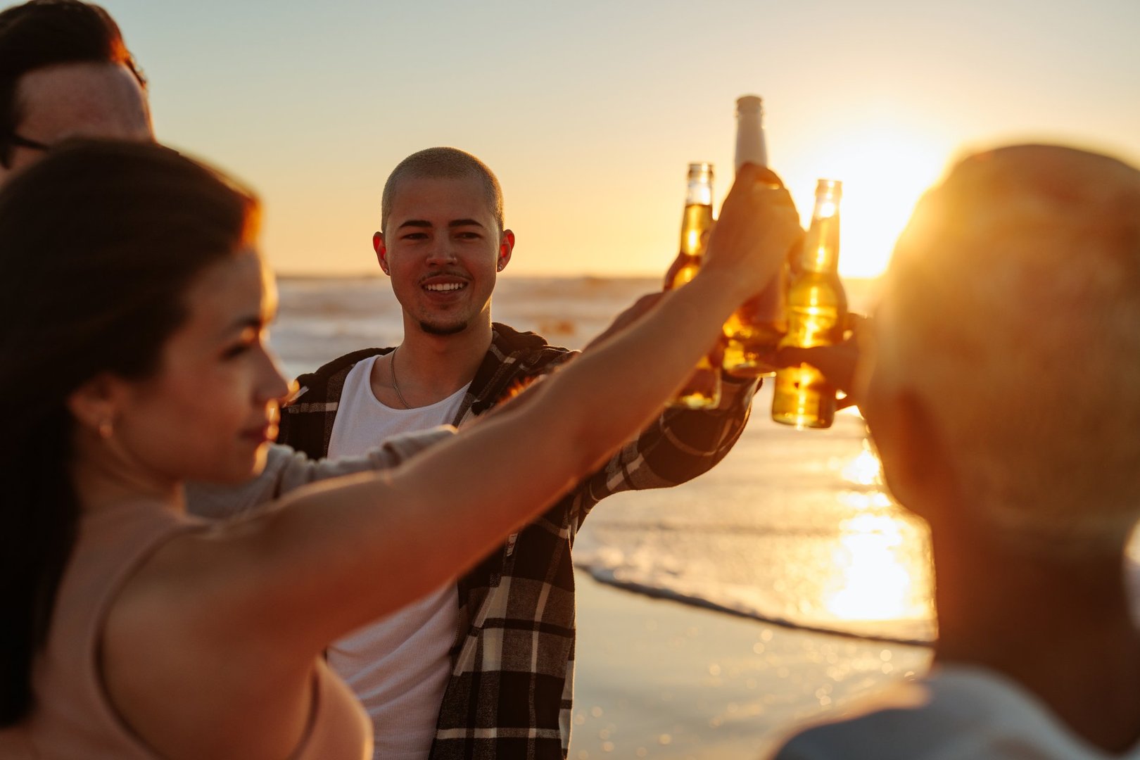 Group of friends toasting with beer bottles at the beach, enjoying a beautiful sunset together