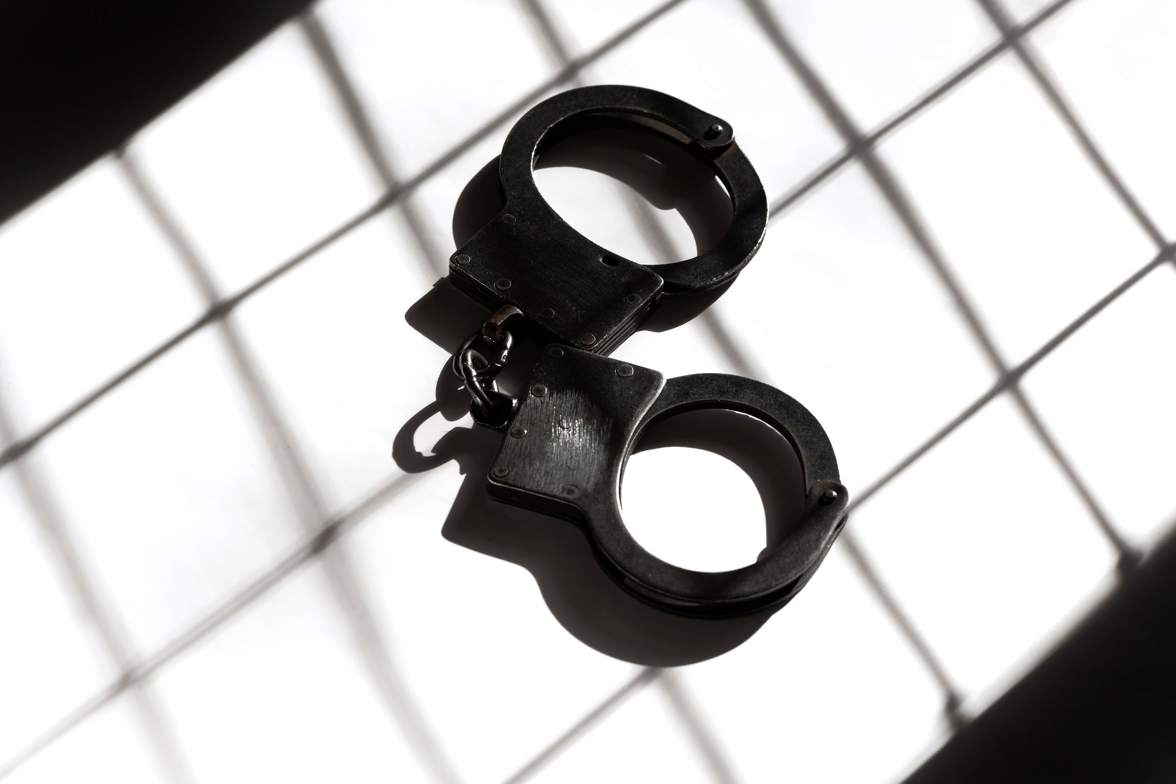 Black steel handcuffs against the background of the shadow of the bars