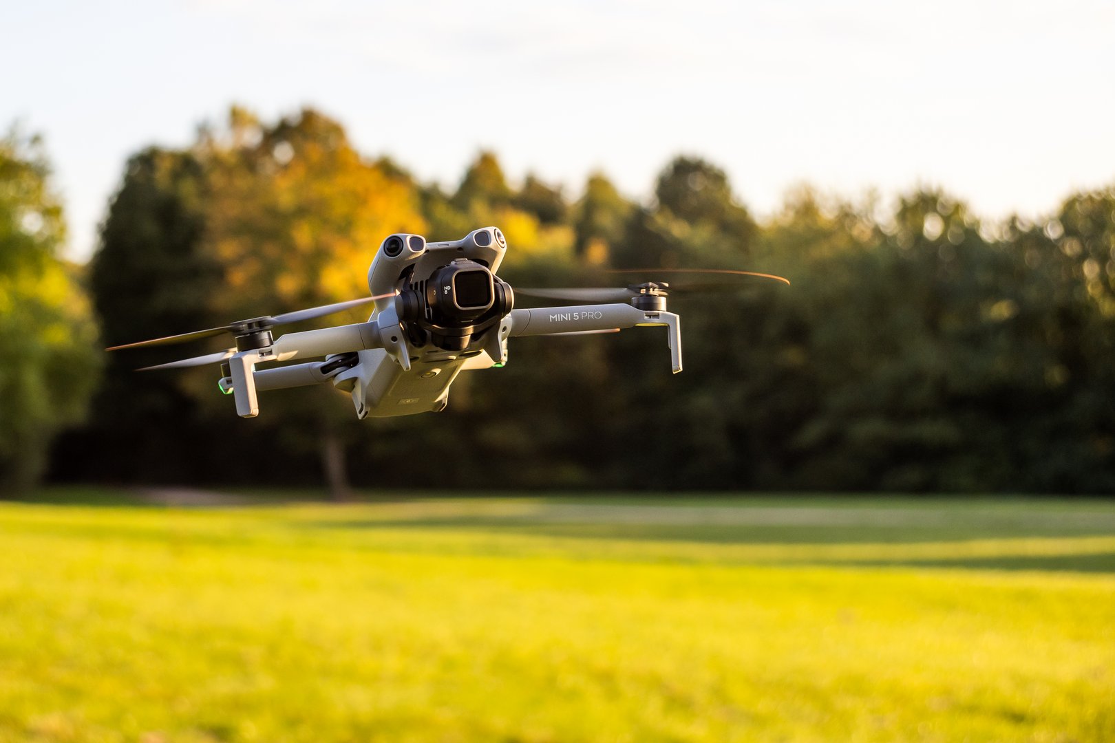 Hamburg, Germany - September 30, 2025: DJI Mini 5 Pro Lightweight Camera Drone in Flight over Green Field during Golden Hour - Close, Horizontal Format