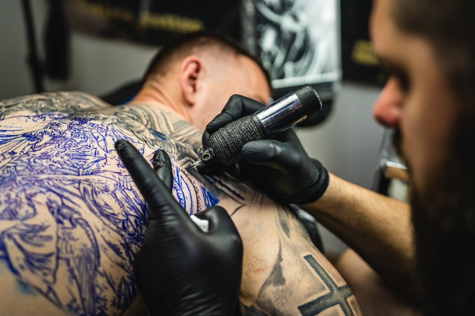 Professional master tattoo artist drawing tattoos picture on man's back using machine wearing black gloves at studio salon body art