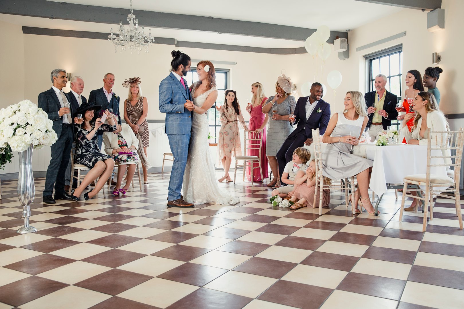 Beautiful couple are sharing their first dance on their wedding day. All of their guests are sitting around the dancefloor watching them.