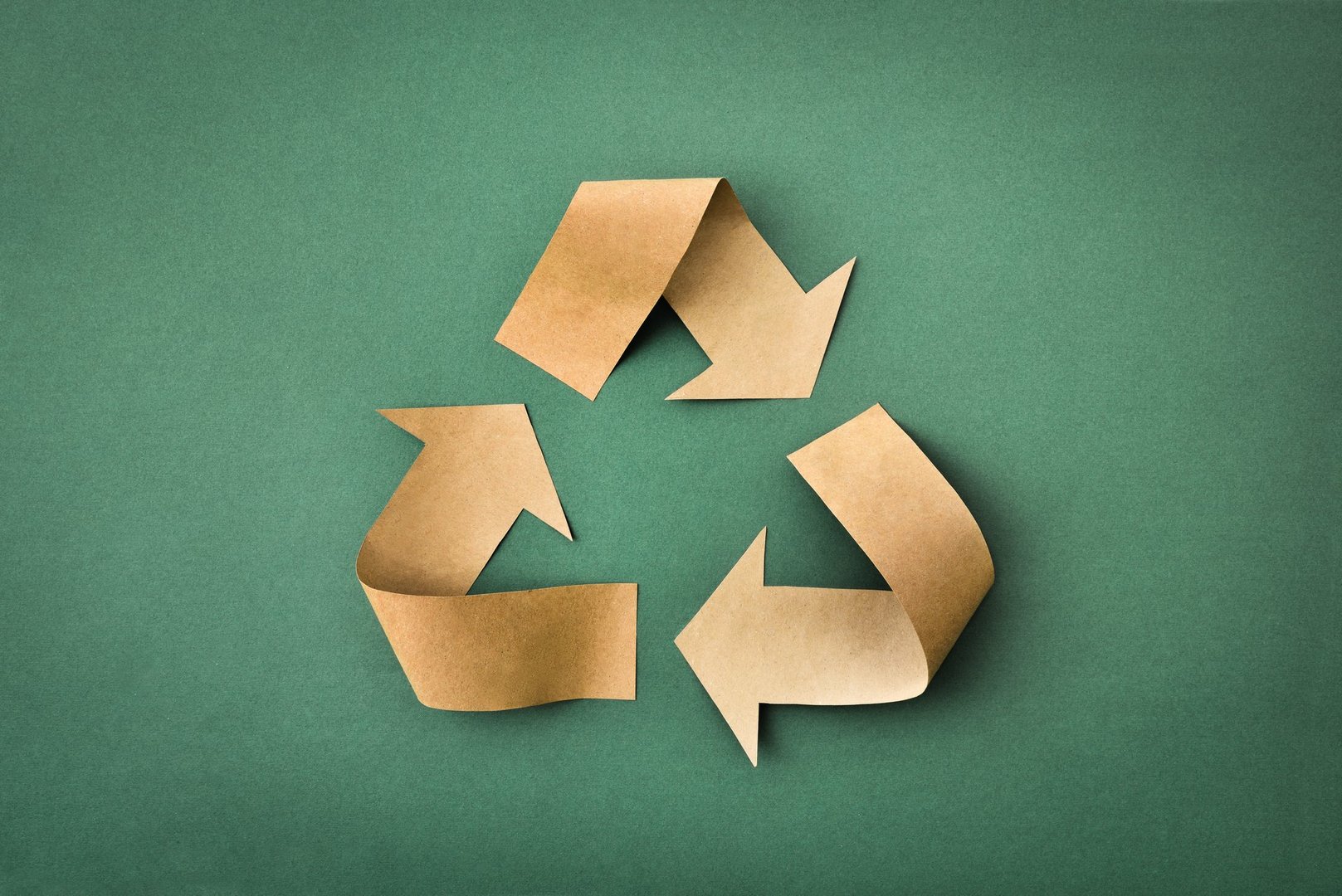 Recycling symbol with arrows made of brown paper on a green textured background. Top view.