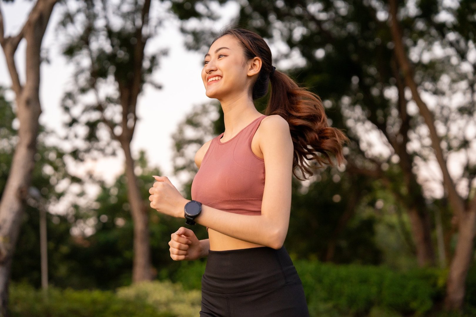 Happy slim woman wearing sportswear jogging in the city at sunrise. Young beautiful asian female in sports bra running outdoor. Workout exercise in the morning. Healthy and active lifestyle concept.