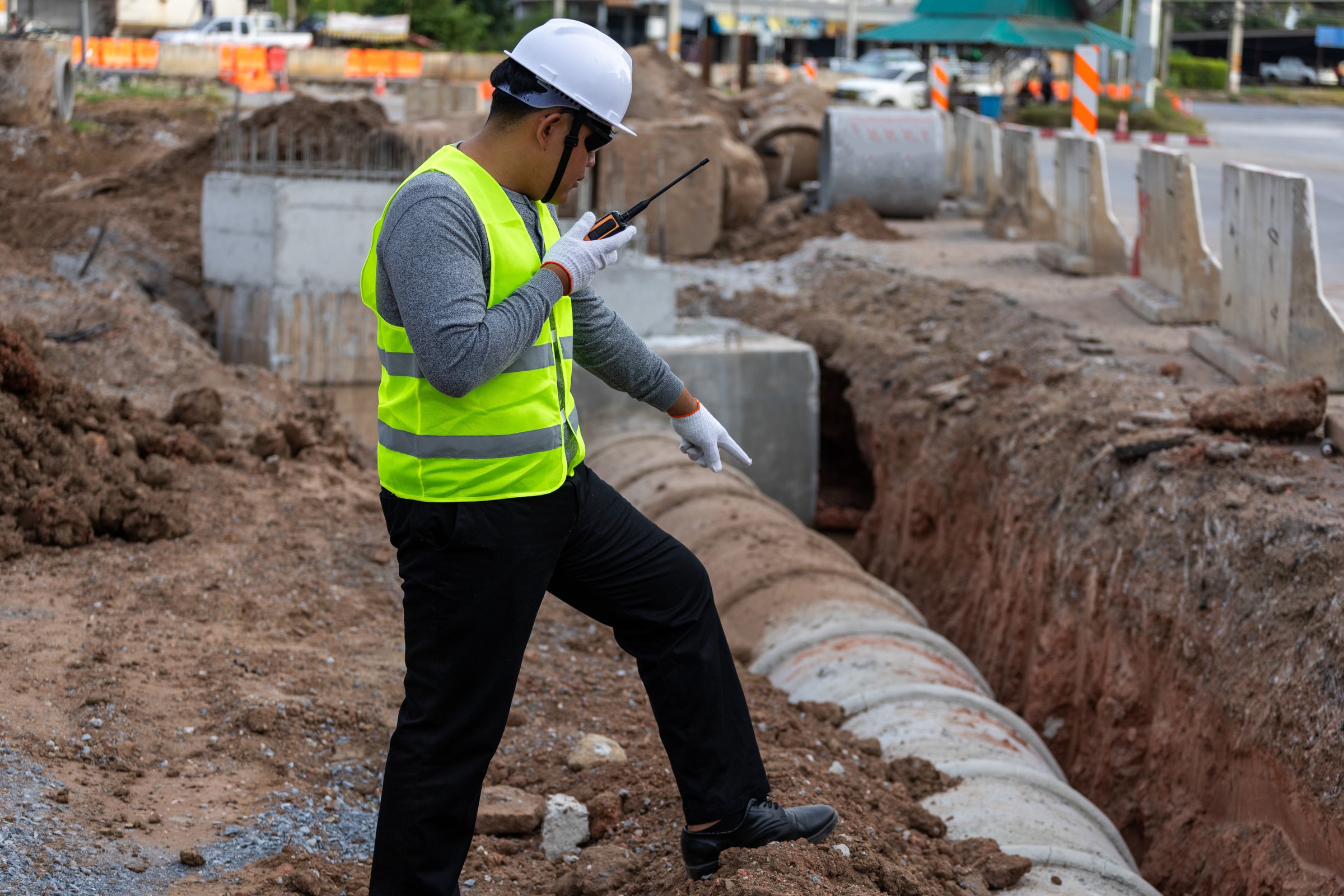 Civil engineer supervising the installation of concrete drainage pipes at a roadside construction site.