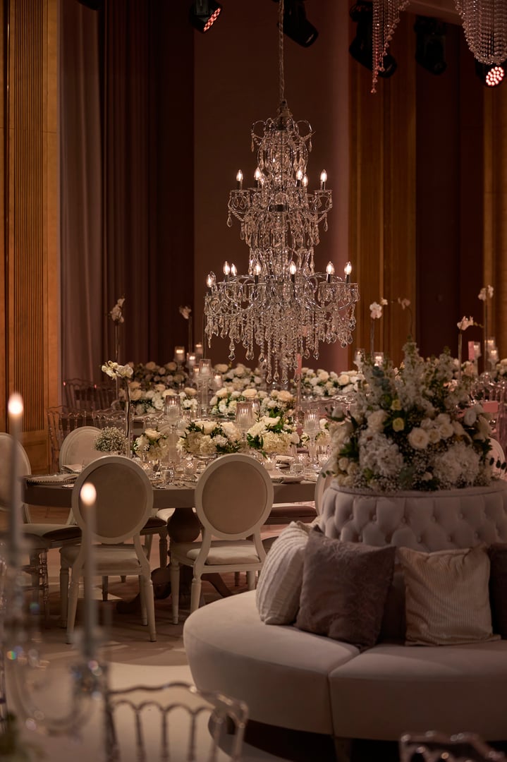 An exquisite close-up of a luxurious wedding table setup featuring a stunning crystal chandelier, elegant floral arrangements, and candlelit decorations. Perfect for showcasing wedding inspiration, event design, or luxury dining themes.