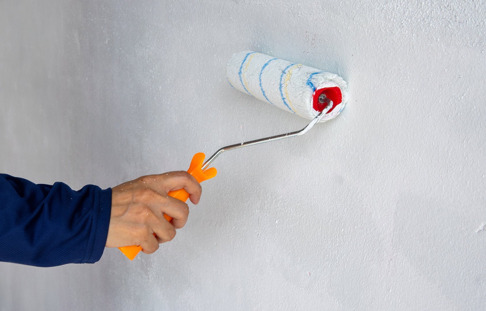 A close-up photo of hand painting a blank white wall with a paint roller. Copy space for text. Home improvement and renovation concept.