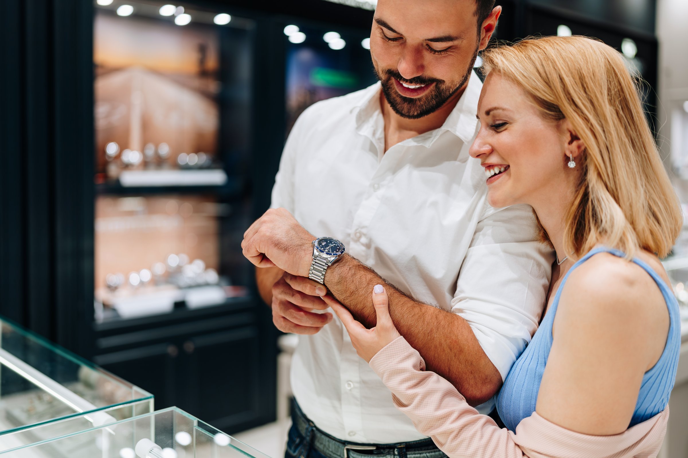 Happy couple smiling and enjoying their shopping experience while trying on a luxurious wristwatch in a jewelry store, celebrating their love and togetherness