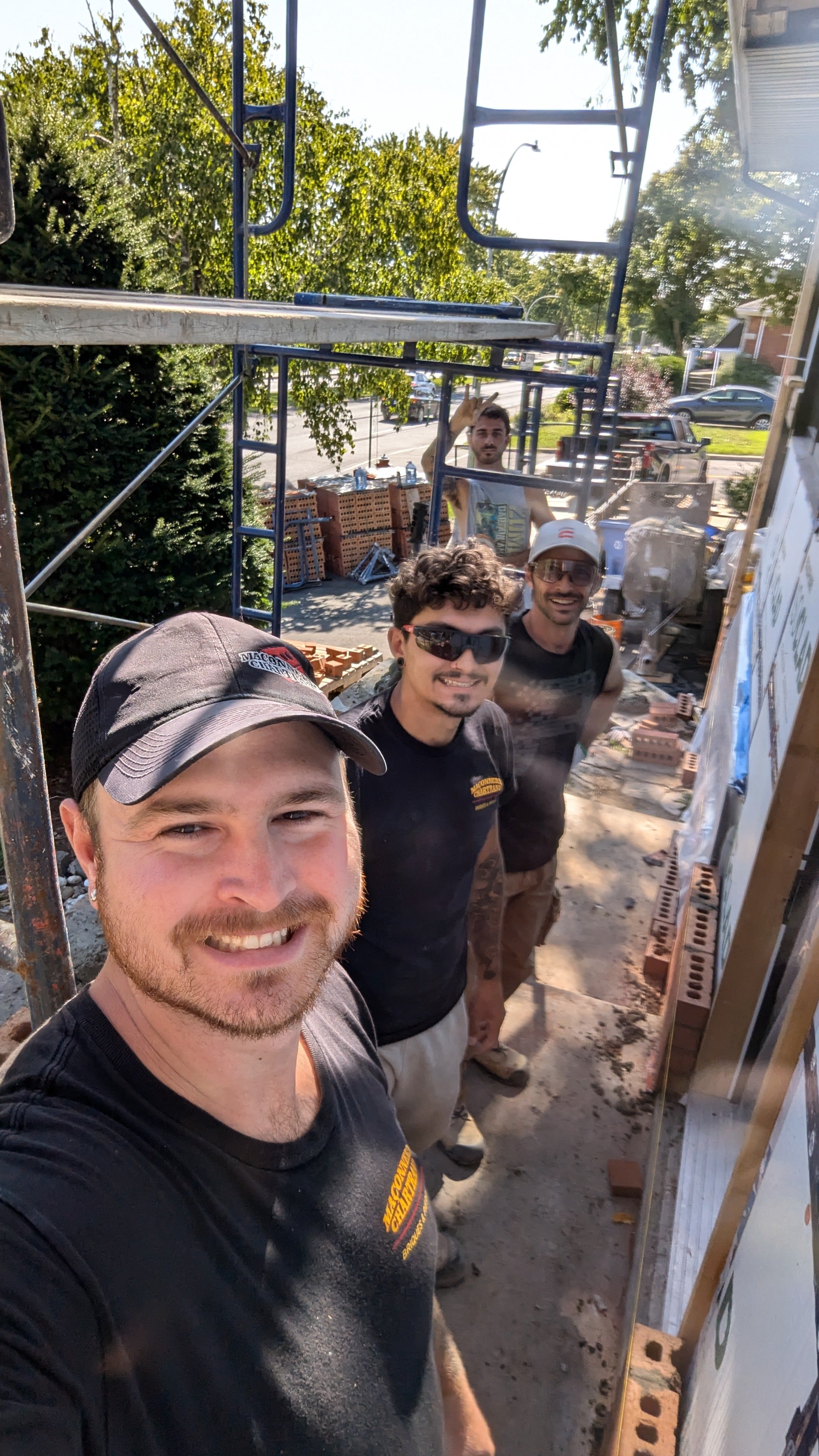 Four construction workers smiling at a building site with scaffolding and bricks in the background.