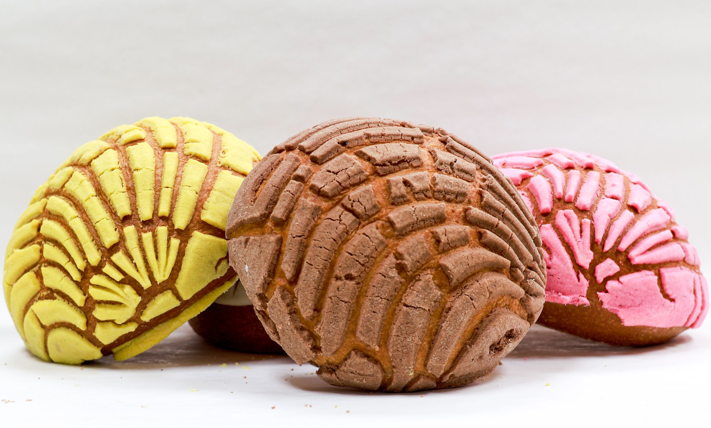 These conchas, a type of Mexican sweet bread. They are popular in Mexican bakeries and are known for their fluffy interior and a distinctive, crunchy topping that is often shaped like a seashell, which is what concha means in Spanish. Each one can have different flavors or colors, as seen in the image.
