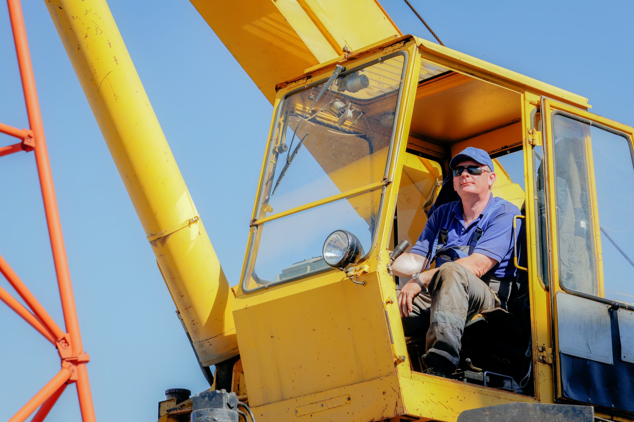 A construction worker operating a yellow crane on site, wearing a blue shirt and hard hat, illustrating machinery control, operations, and construction work.