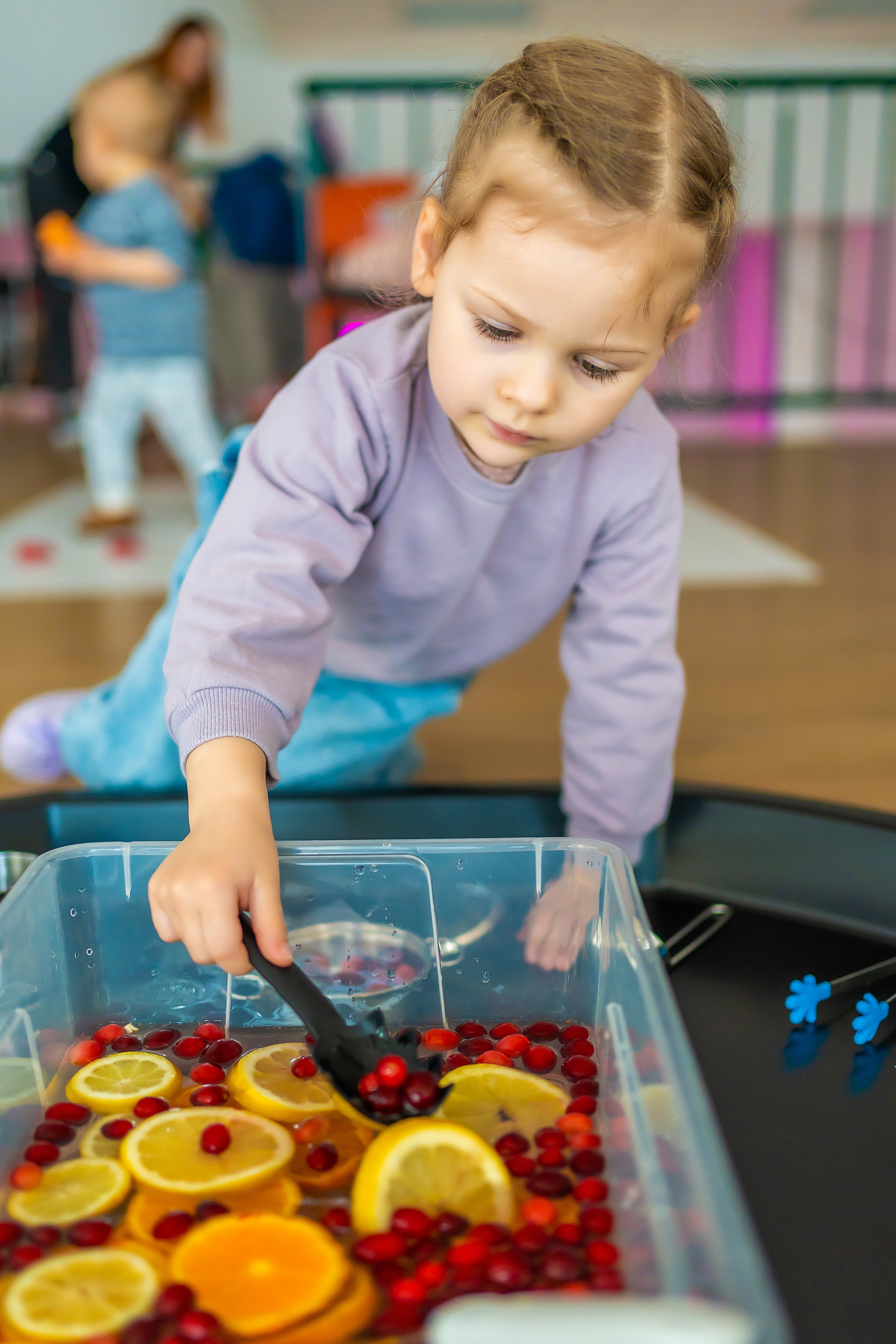 Little girl playing in handmade fruit bar with kitchenware, berries and citrus fruits. Sensory development and experiences, themed activities with children, fine motor skills development.