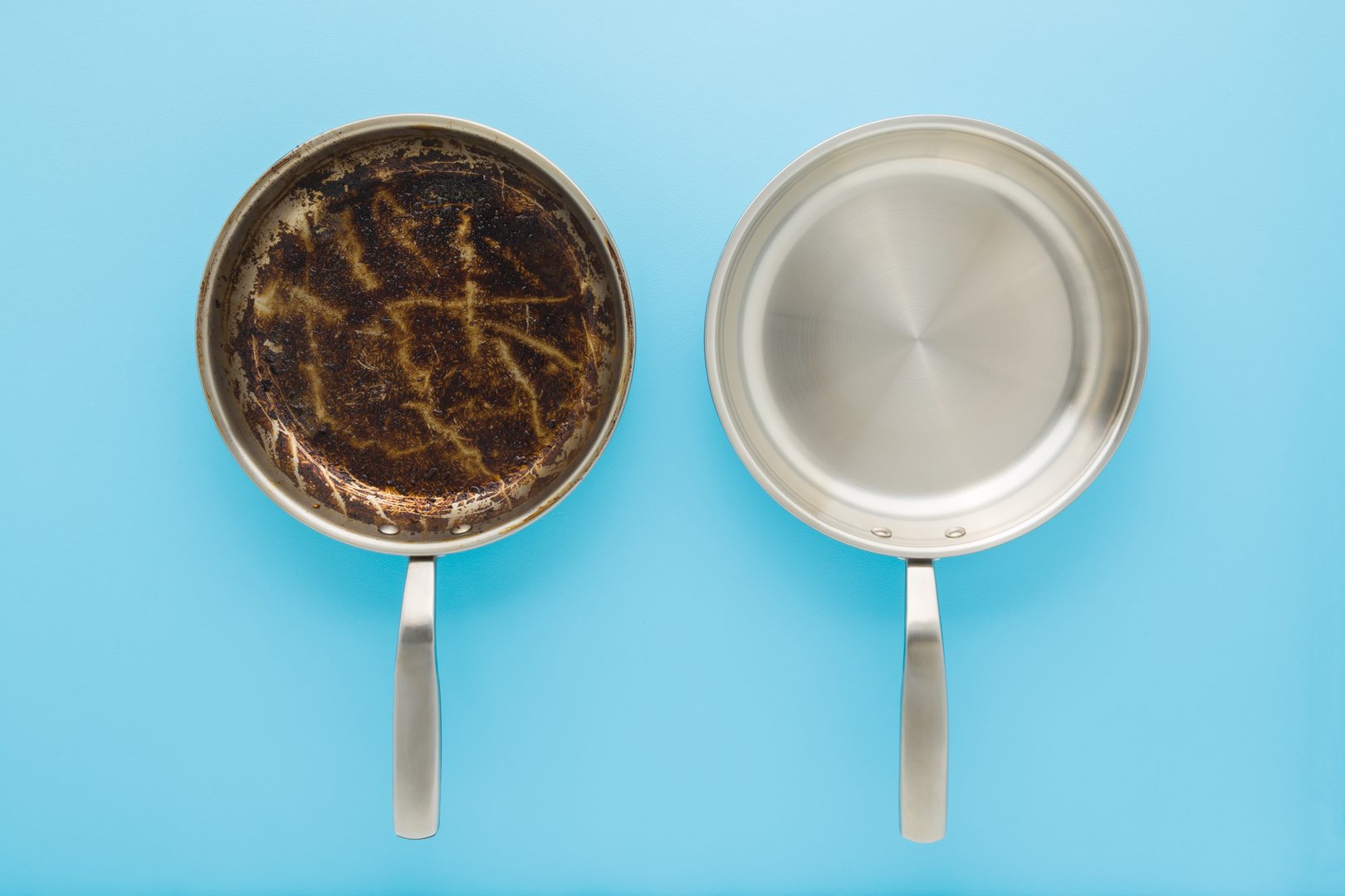 Dirty oily and clean stainless frying pans on light blue table background. Closeup. Pastel color. Removing burn grease stain. Compare two objects. Top down view.