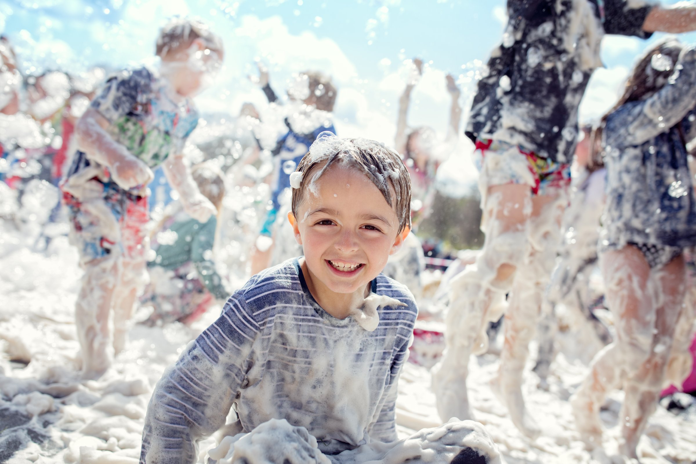 Boy smiling and laughing covered in soap suds at a summer foam party