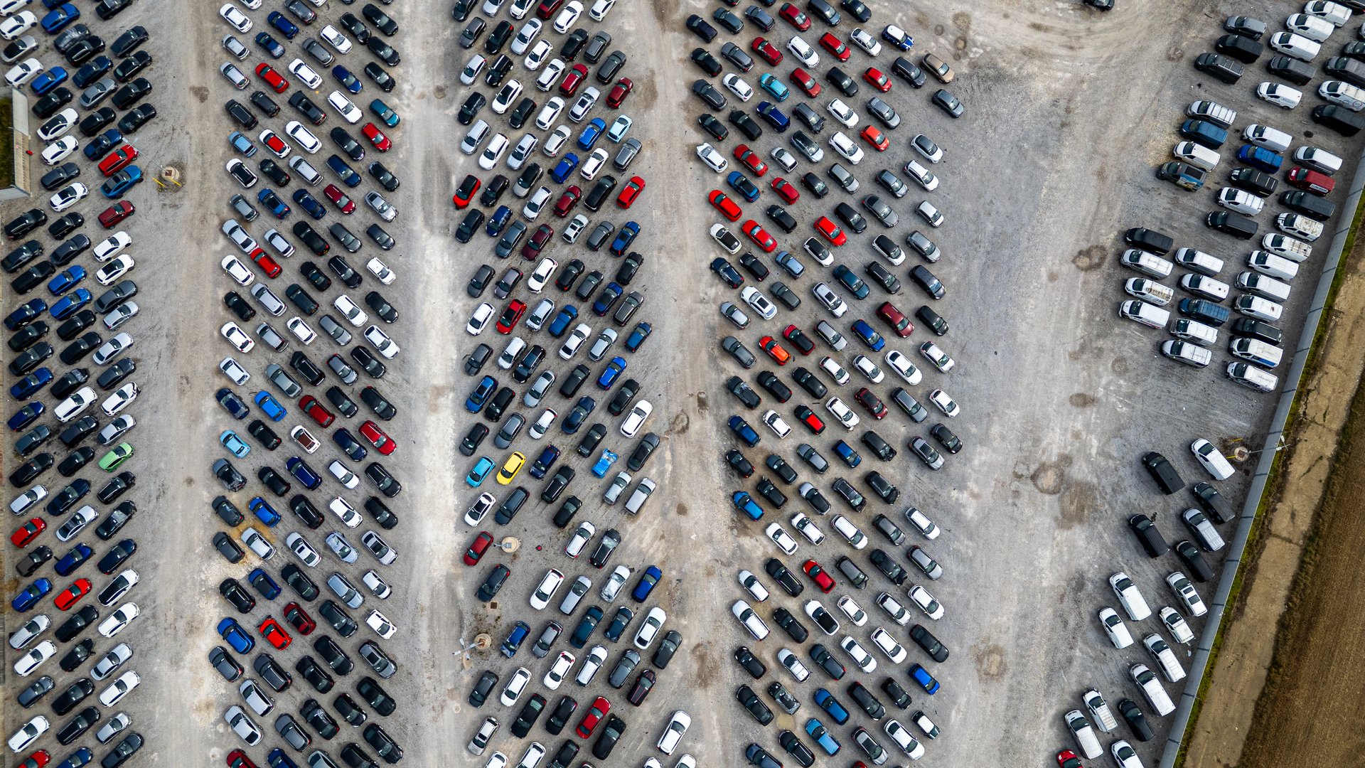 An aerial view of a large outdoor car storage lot filled with numerous cars parked in rows on a gravel surface  at Copart yard in York, UK.