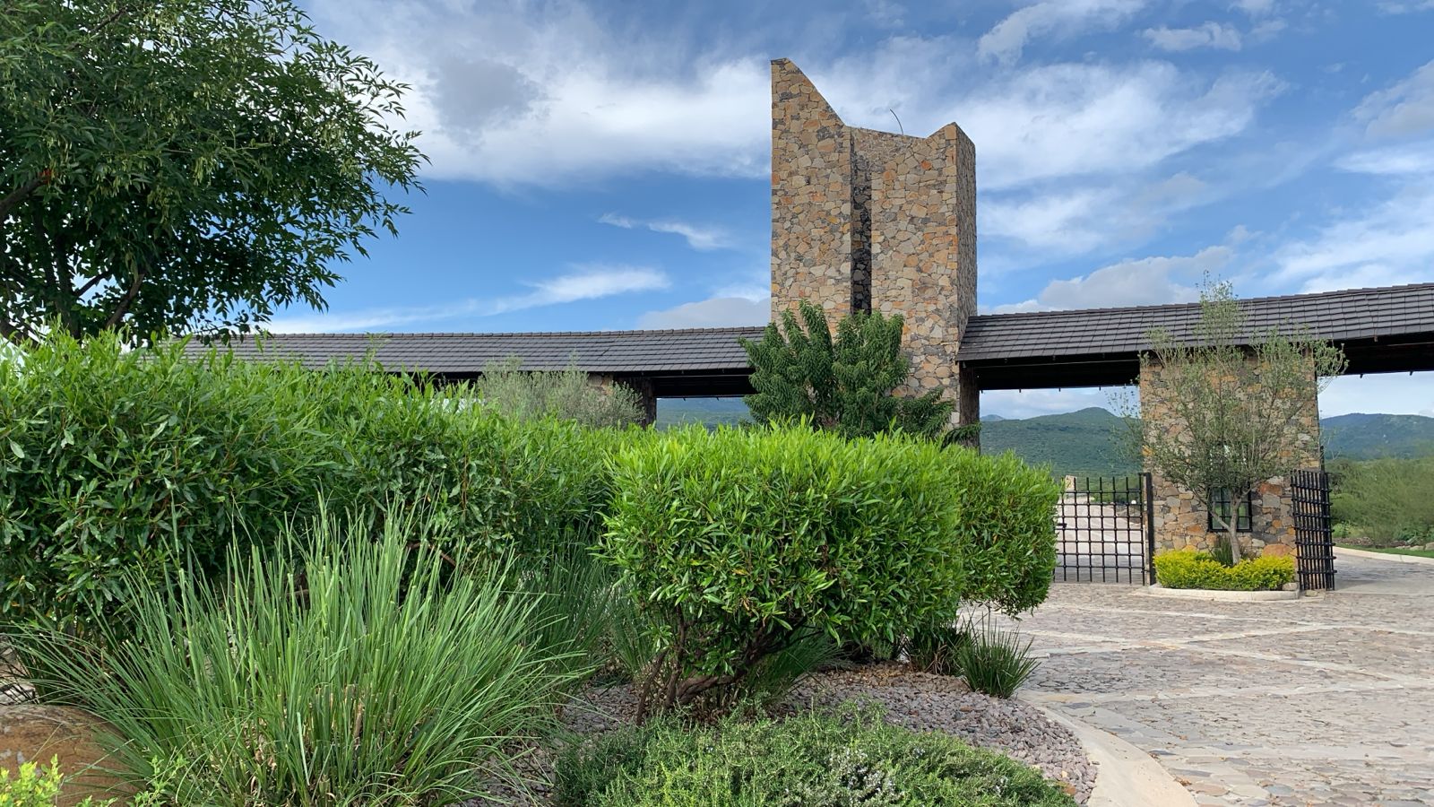 Modern stone building with a tall tower set against a blue sky, surrounded by lush greenery and a cobblestone path.