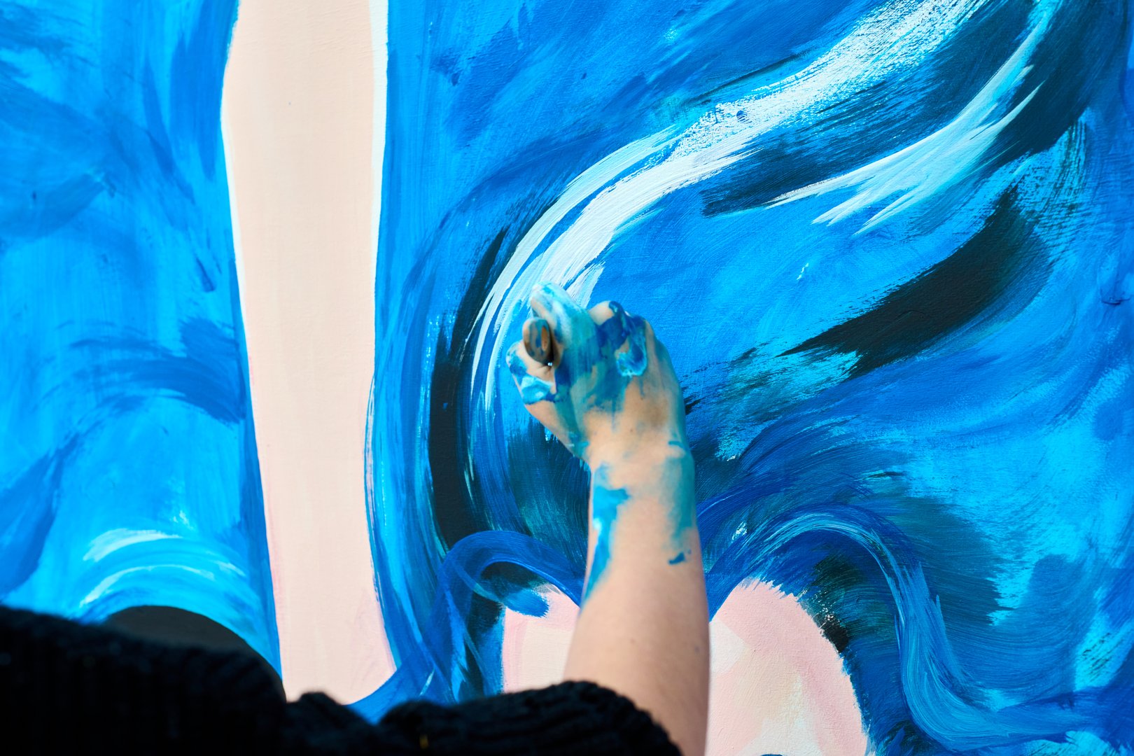 Young adult female with black hair paints dynamic blue abstract art. Close-up shot highlights energetic brushstrokes, vibrant color palette, and expressive creativity