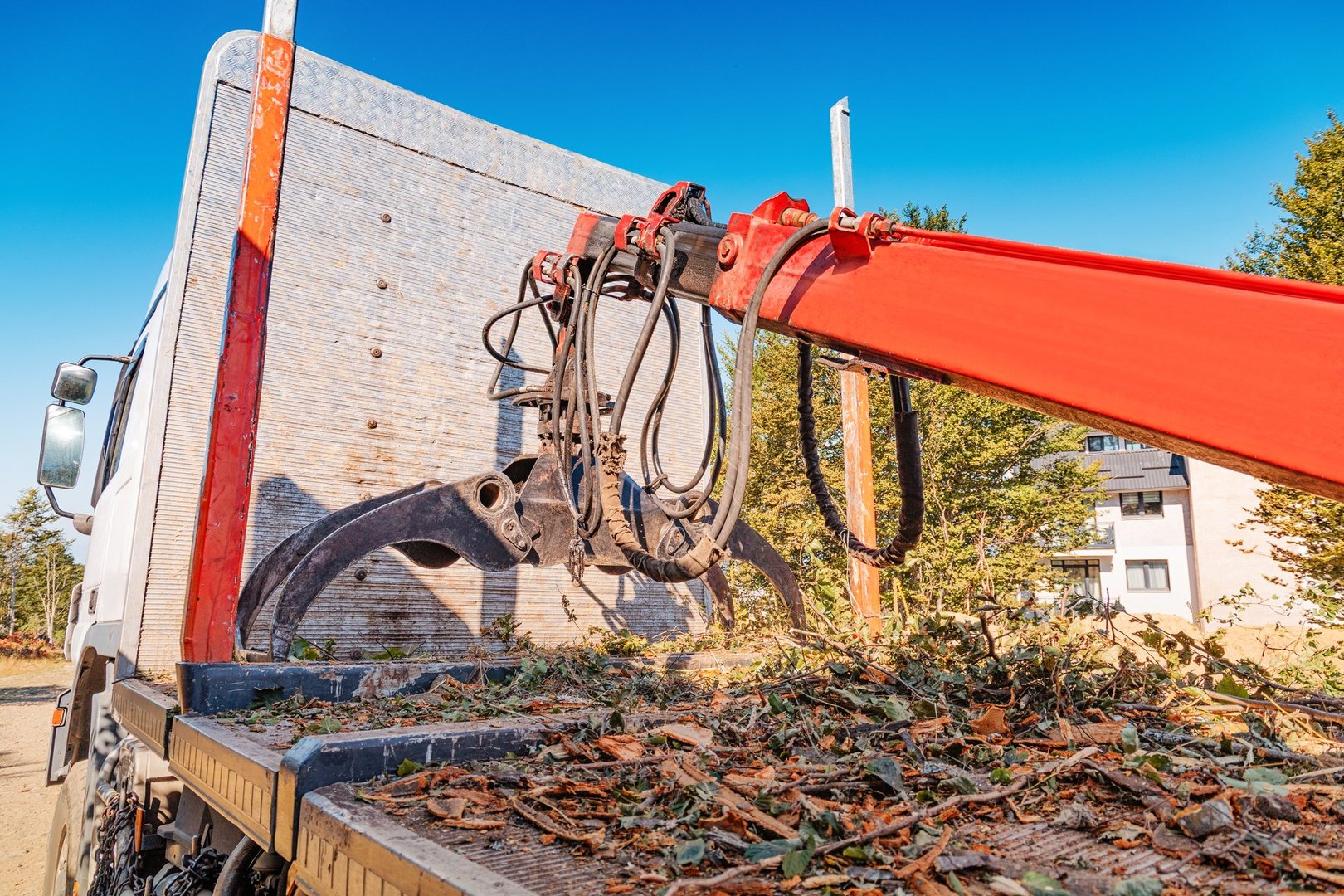 Logging truck equipped with a hydraulic crane and grapple attachment loading wood waste and chippings, managing forestry debris