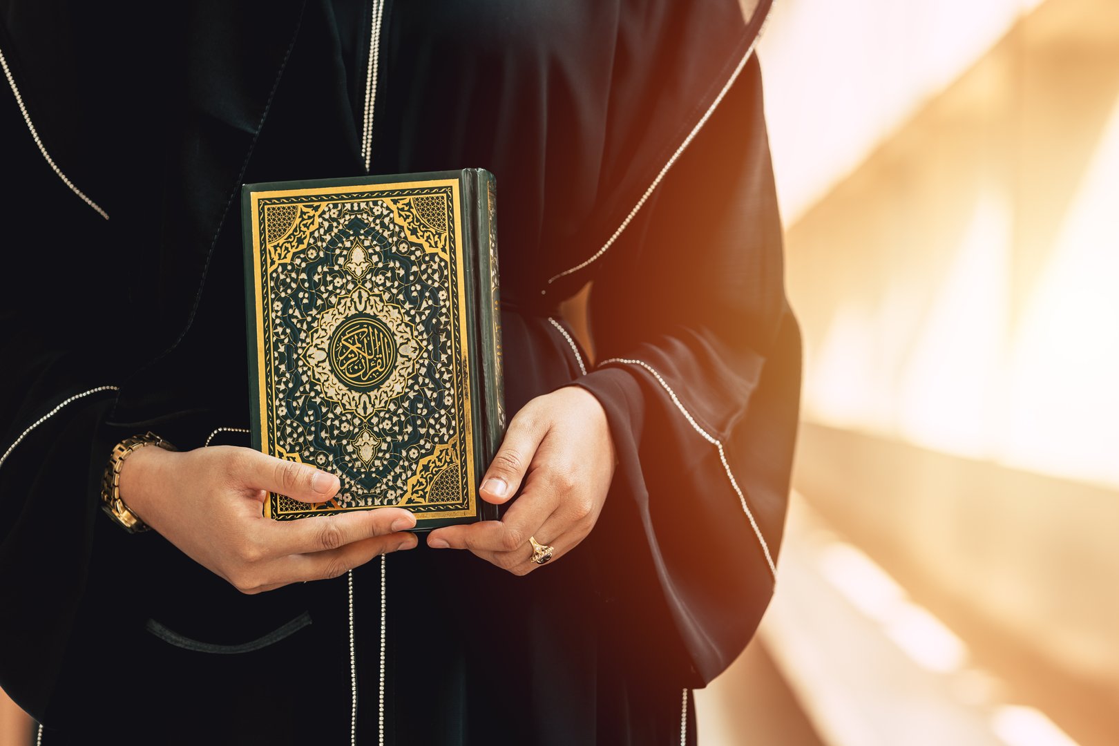Holy Quran book cover with arabic calligraphy translate meaning of Al Quran. Closeup Arab people hand holding Quran muslim book.