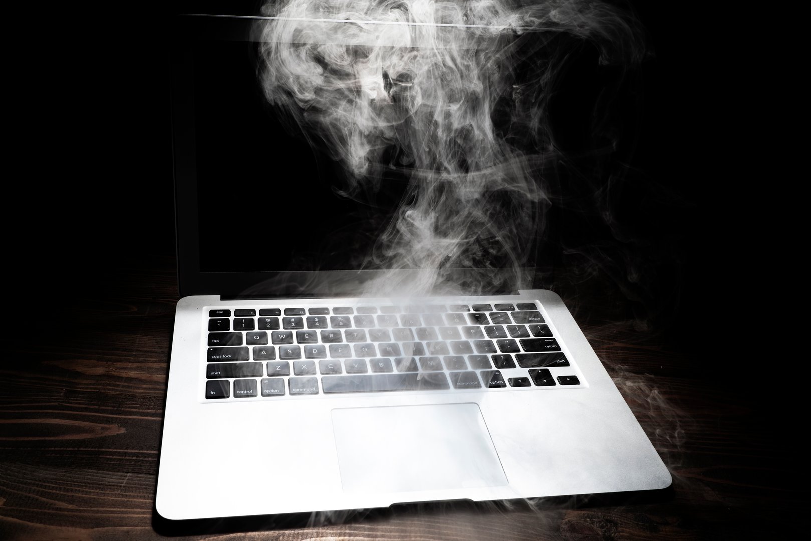 A broken laptop smoked on the wooden table. Breakdown gadget concept