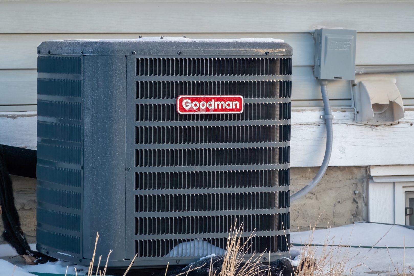 Calgary, Alberta, Canada. Jan 20, 2025. A large, grey Goodman air conditioning unit sits on a snowy lawn