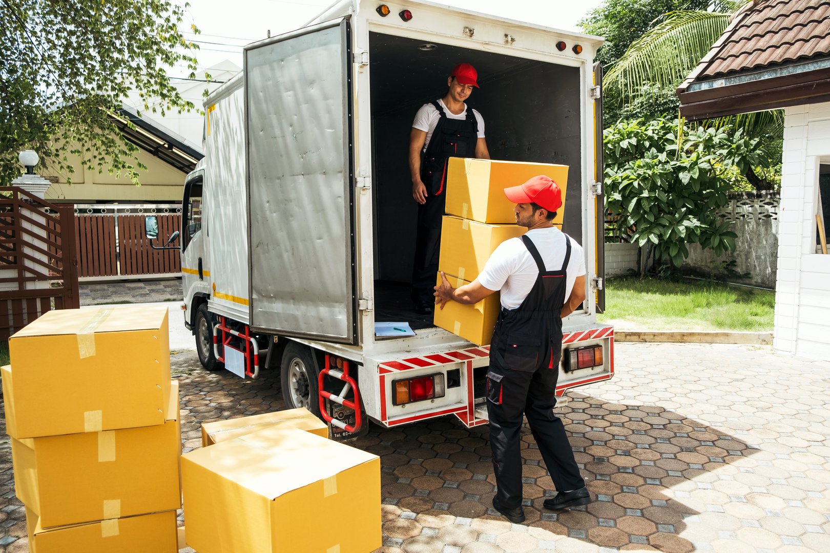 Asian and Caucasian workers in uniform unloading cardboard boxes from the truck. Delivery men unloading boxes and check the checklist with their coworkers. Professional delivery and moving service.