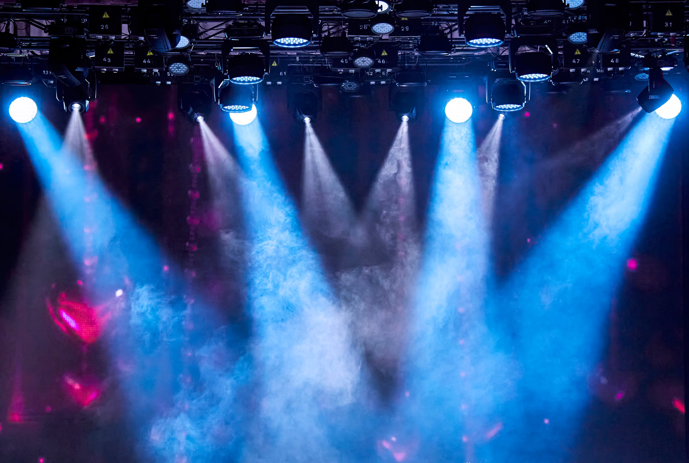 The photo shows a dark background with several bright stage spotlights shining through the smoke, creating a dramatic and vibrant atmosphere. Perfect for use as a background for a variety of projects.