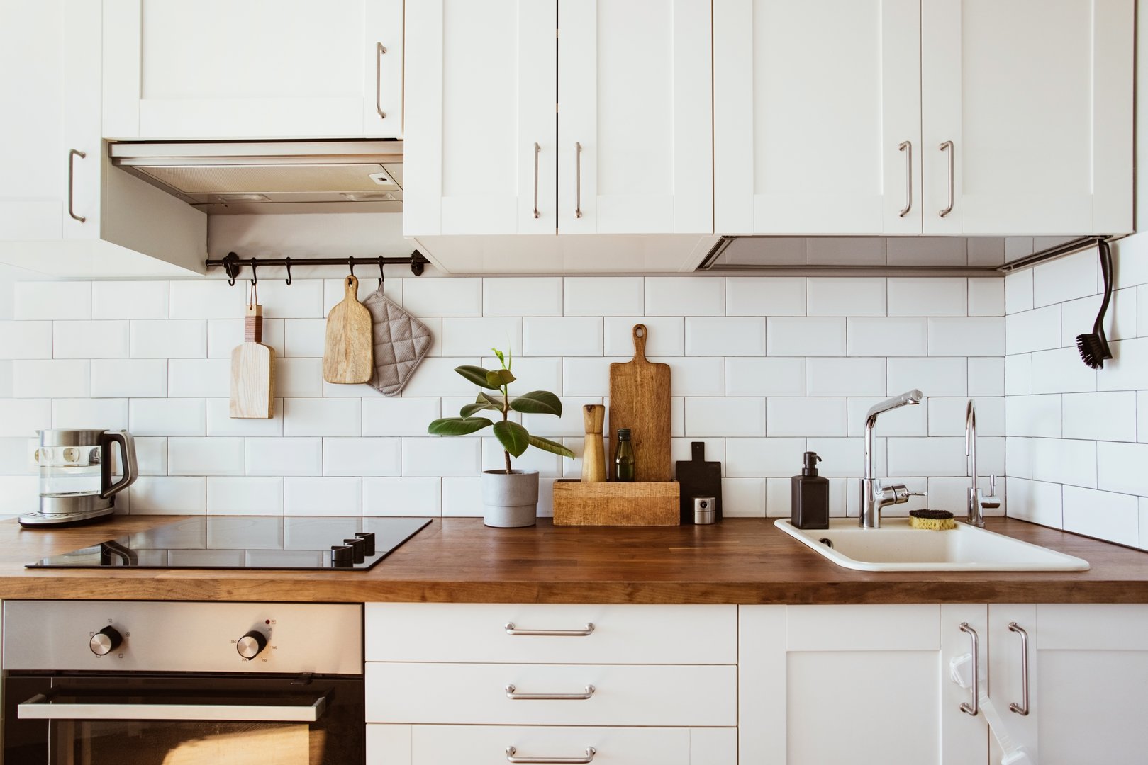Kitchen brass utensils, chef accessories. Hanging kitchen with white tiles wall and wood tabletop.Green plant on kitchen background side view
