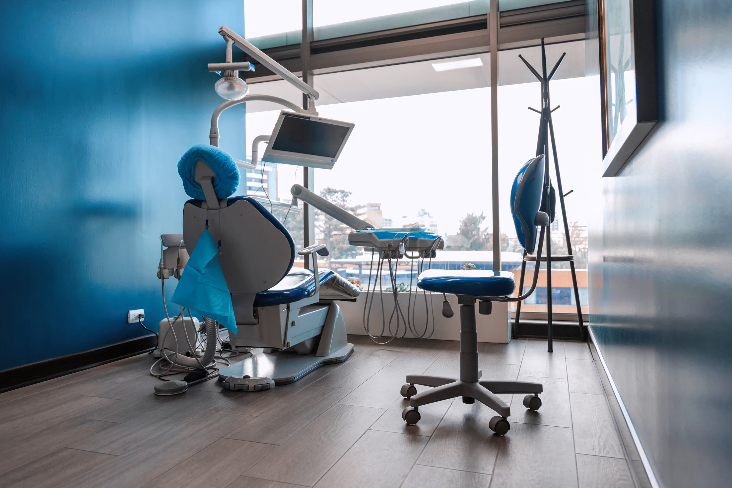 Contemporary dental chair setup in a clinic with tools and monitor near large window on rainy day. Concept of modern dentistry, patient care, and clean medical environment.