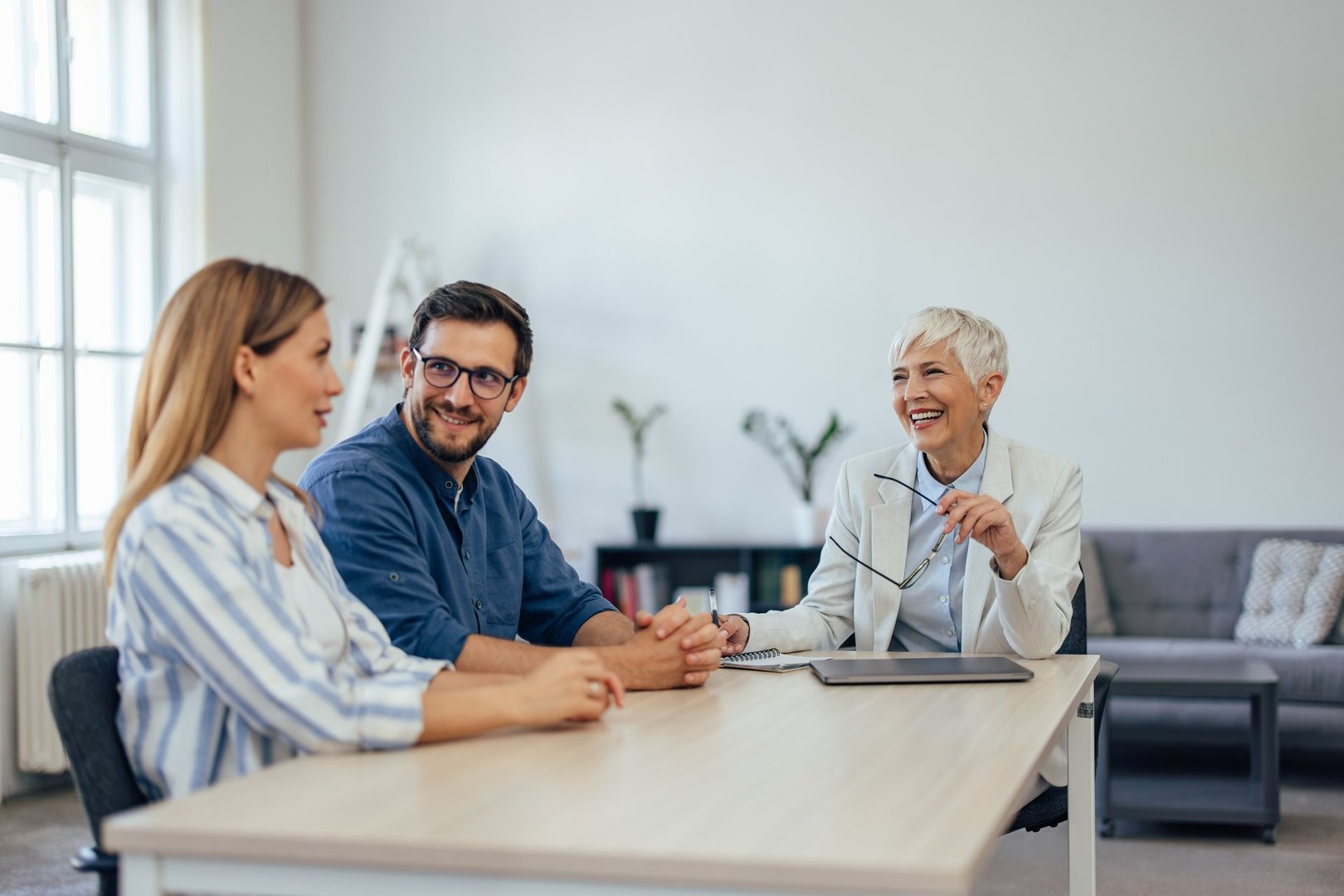 Smiling female insurance agent, holding glasses and listening to a young couple.