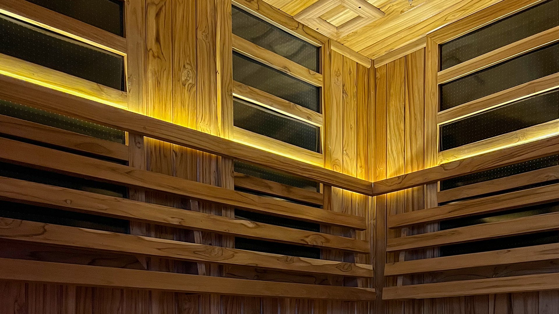 Wooden sauna interior with horizontal panels and warm ambient lighting along the walls and ceiling.