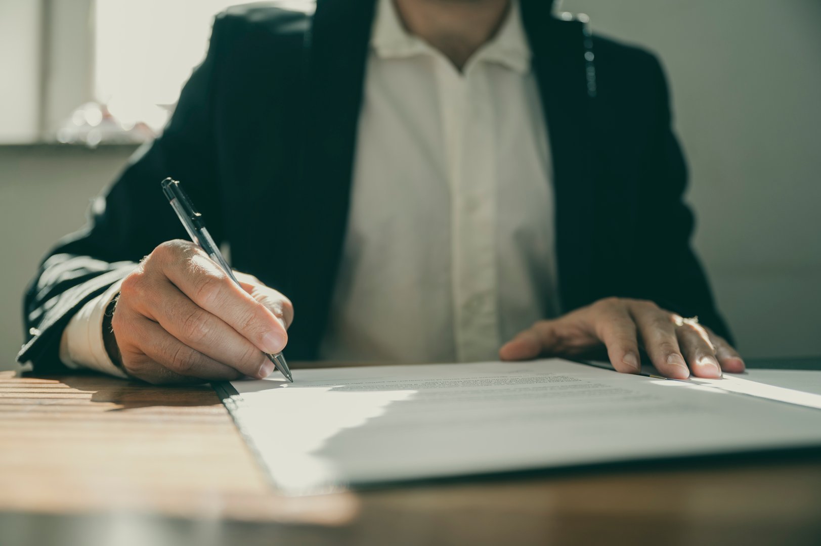 Front view of a torso of a businessman or a lawyer signing a contract or document sitting at his office desk.
