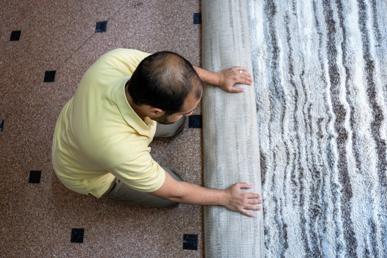 A person carefully rolls up a plush carpet in a modern living space, emphasizing neatness and organization. The scene suggests home maintenance and interior decor