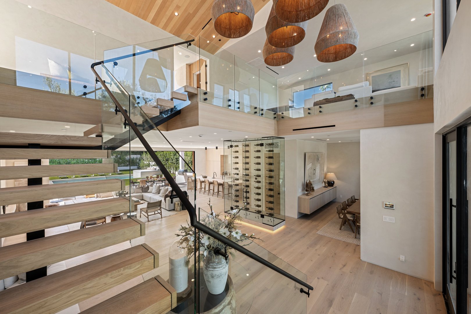 Modern open-concept living space with glass railings, wooden floors, and elegant lighting, featuring a wine cellar and spacious seating area.